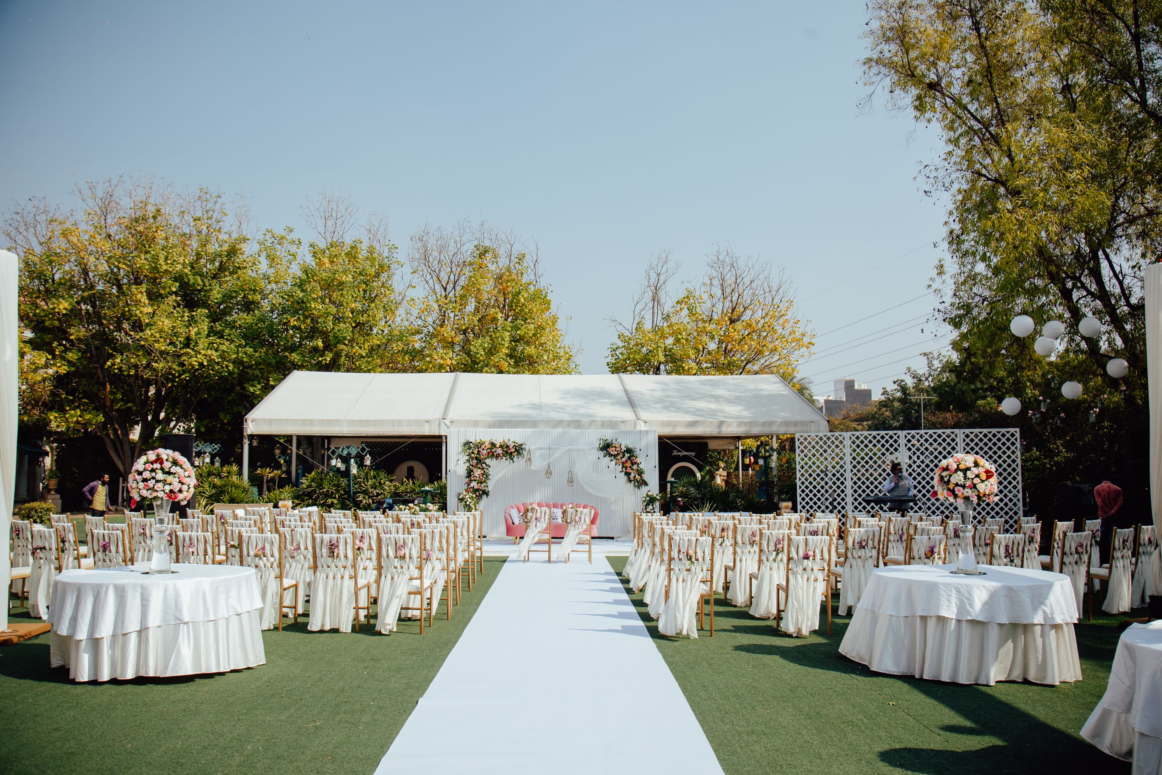 A sweeping, cinematic wide shot of a luxury outdoor wedding set at sunset on a grand, manicured lawn.